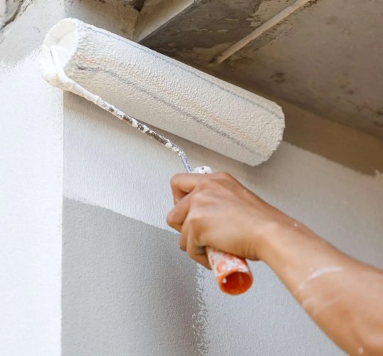 A person painting a wall with a paint roller. A person painting a wall with a paint roller.