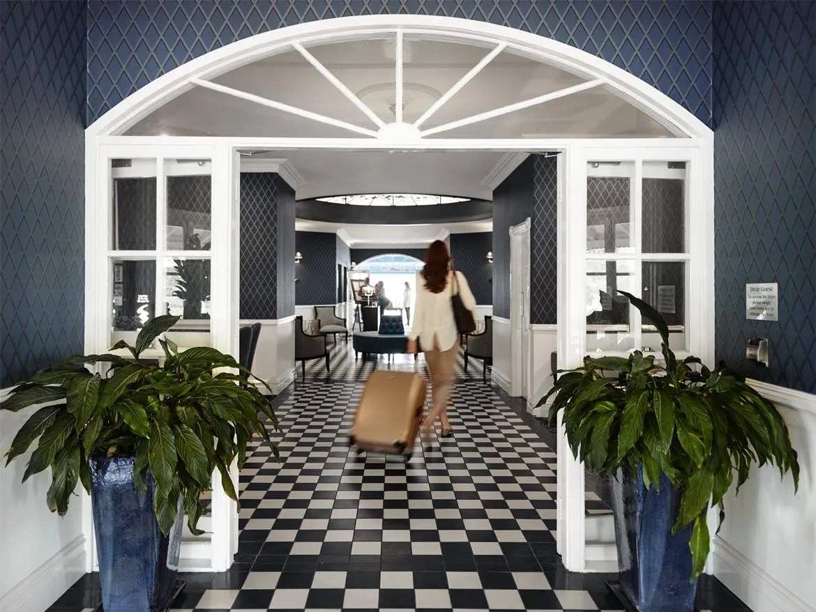 A woman is walking down a hallway with a suitcase.