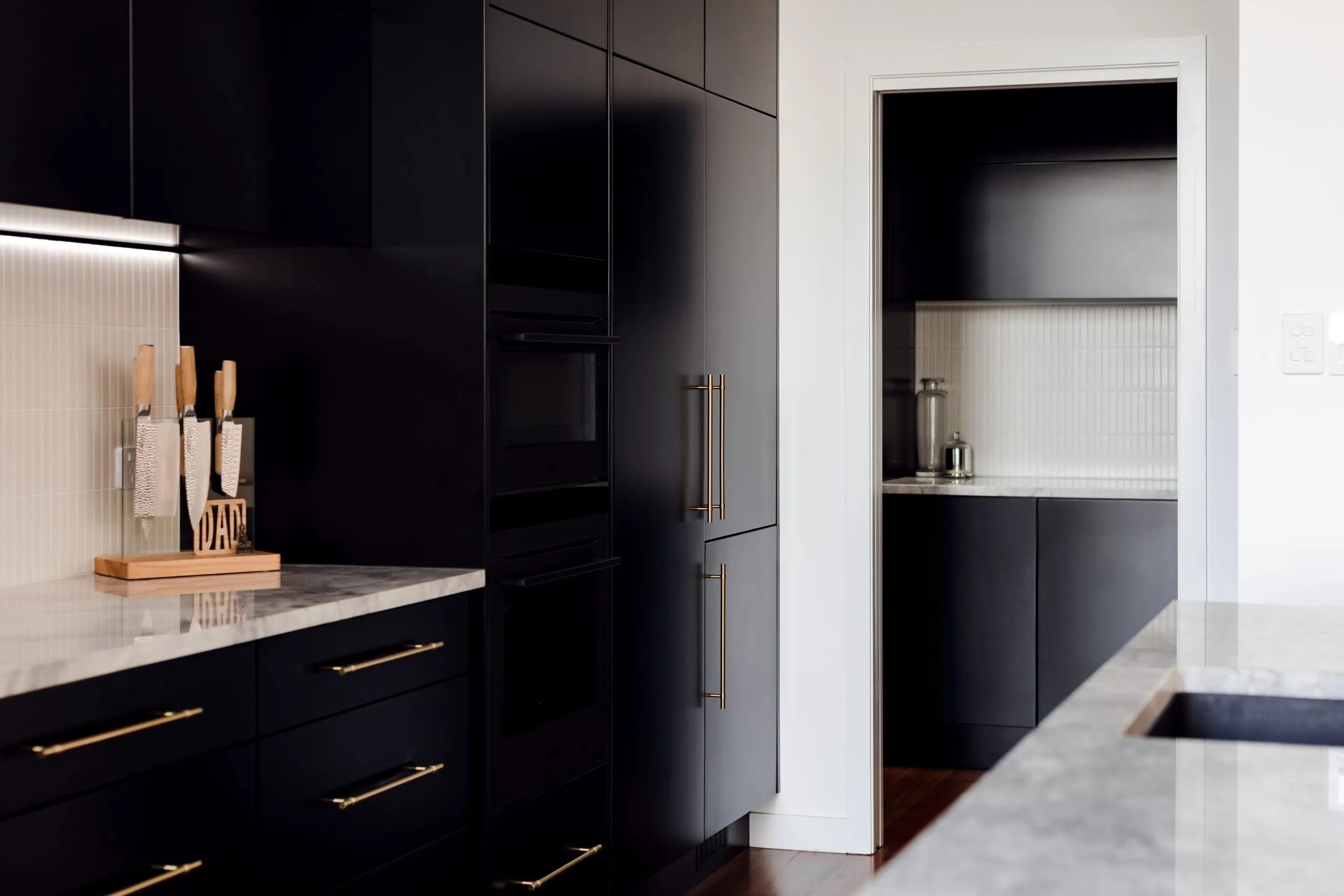 A modern kitchen with black cabinets and marble counter tops.